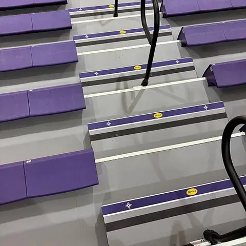 Arena seating steps featuring branded stair nosings and slip-resistant safety inserts installed throughout a stadium seating area.