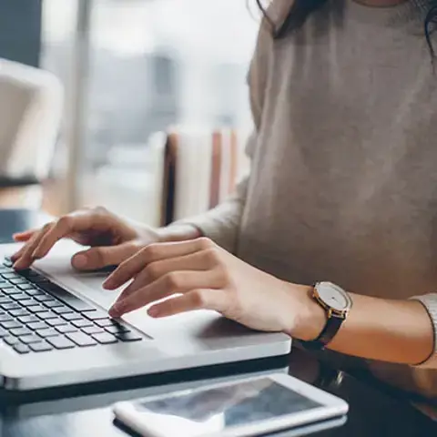 Person working on a laptop at a desk with a smartphone nearby.